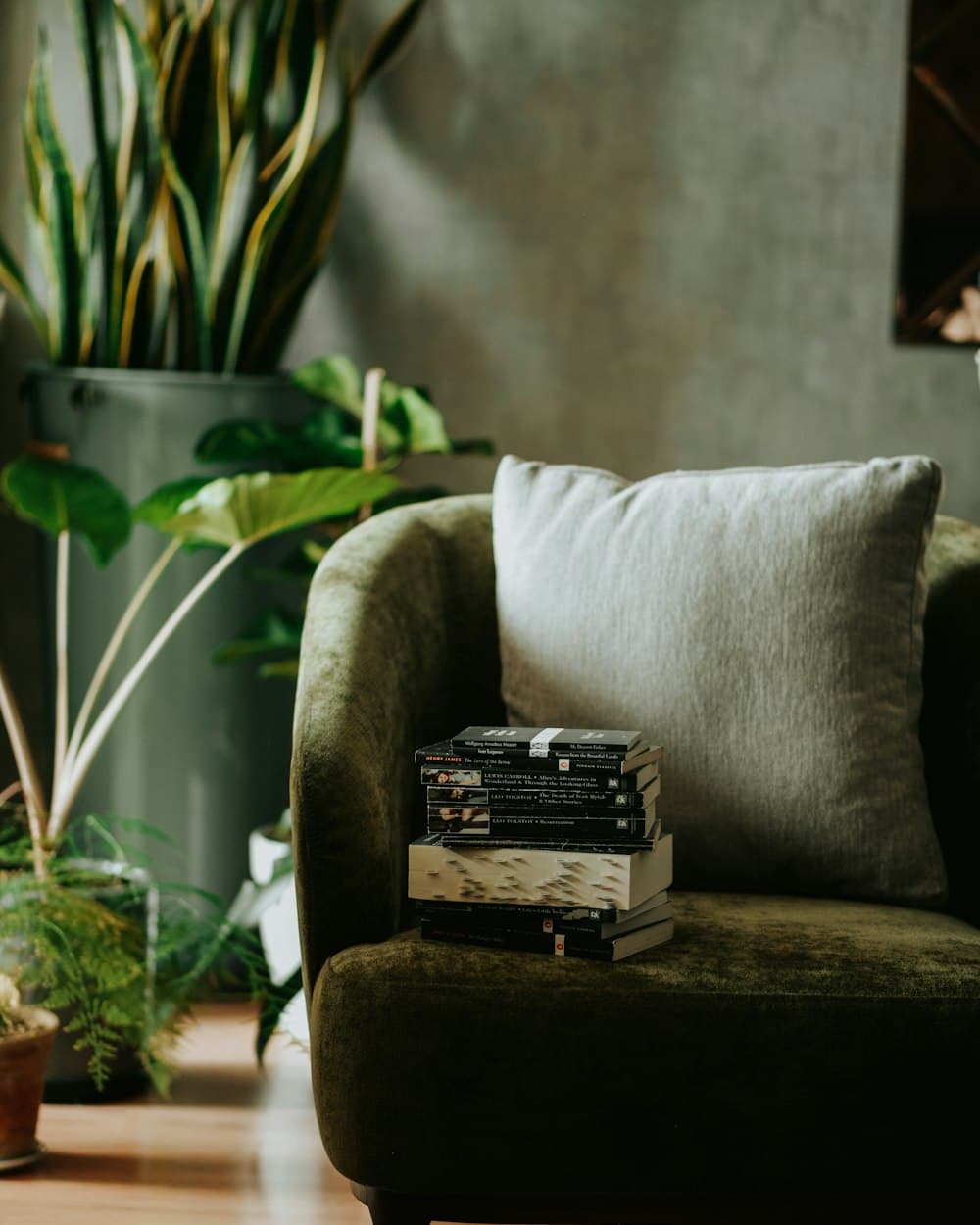 A stack of books on a green armchair next to plants