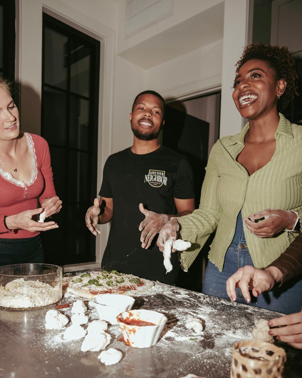 Friends laughing while making pizza together in a kitchen