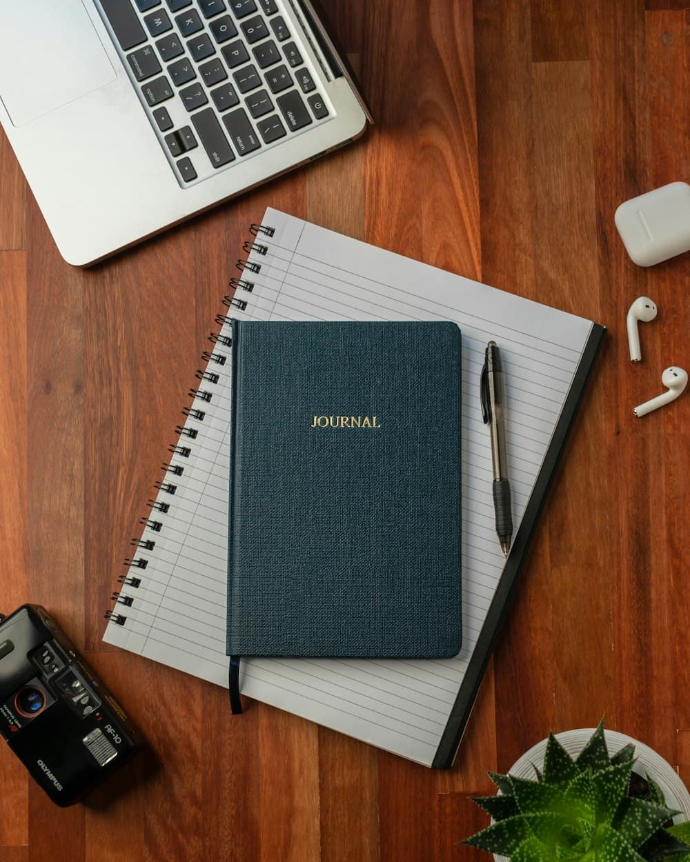 A notebook, pen and laptop on a wooden desk
